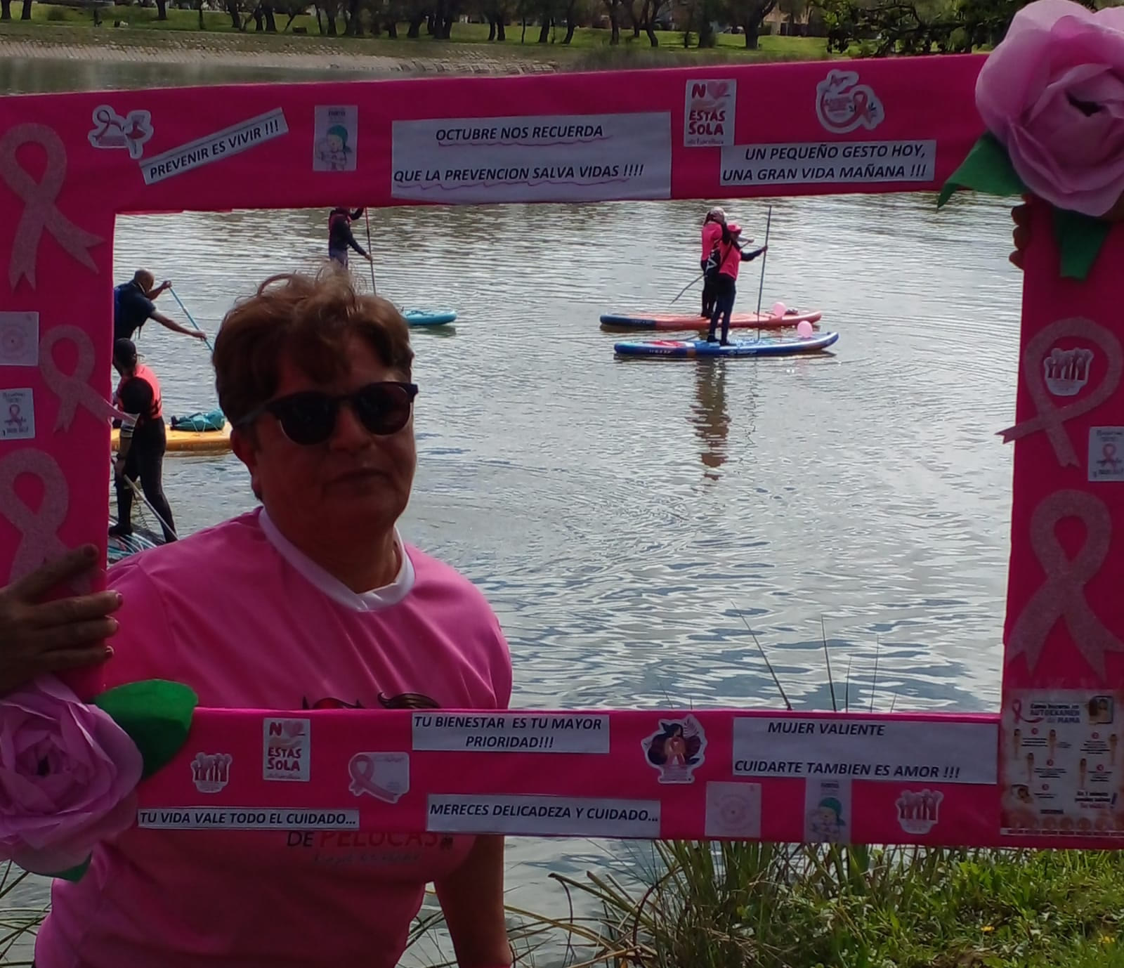 Vecina posa en el marco de la Caminata Rosa junto al río, con palistas de paddle de fondo