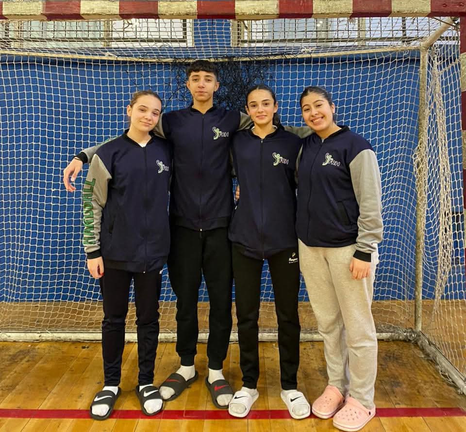 Cuatro jugadores de la Escuela Municipal de Handball de Patagones posan con camperas del equipo delante del arco de un gimnasio