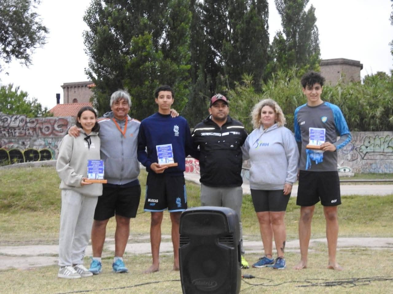 Integrantes de la Escuela Municipal de Handball de Patagones con medallas y placas en un acto al aire libre, junto a dos adultos que las acompañan